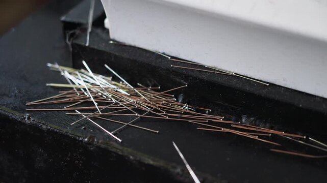 Close-up of sewing machine needles scattered on a work surface, highlighting fine metal detail, textile work environment, and tools used in garment production. Malaysia, UHD.