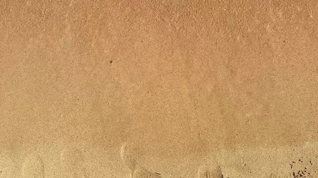 The word Dreams, written in the sand and washed away by gentle waves, demonstrate the fleeting nature of time. On a sunny beach with soft golden sand and clear water.