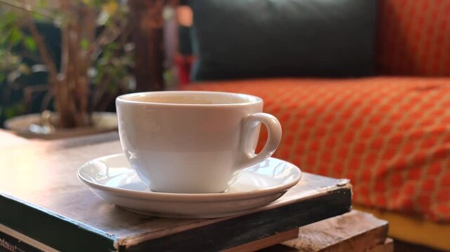 Steam rises from coffee cup on stacked books near couch slow motion clip.