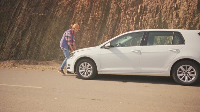 Sunlit rural road where man checks car for faults, Peaceful countryside setting with repairs underway on sunny day
