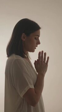 Woman in prayer position with hands clasped in peaceful meditation, vertical shot