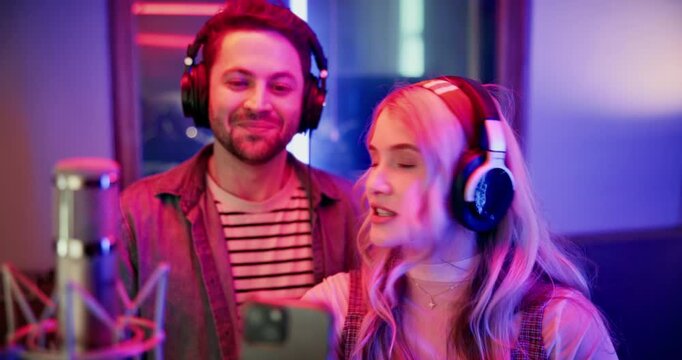 Artist, live stream and team with smartphone in recoding studio, entertainment and talking with fans. Musician, online and people with headphones for content creation, creative and vlog with mobile