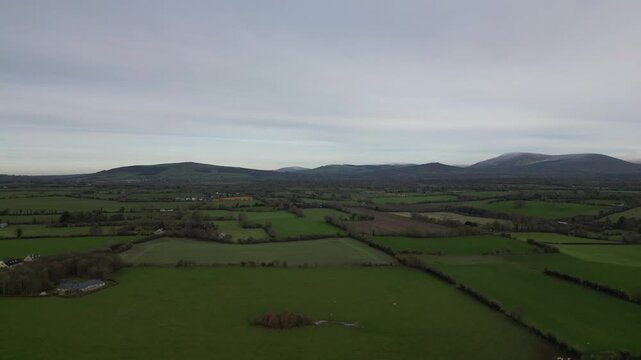 Breathtaking aerial footage of Suir Valley's lush green fields and rolling hills under a moody overcast sky, captured in County Waterford, Ireland. Perfect representation of rural tranquility.