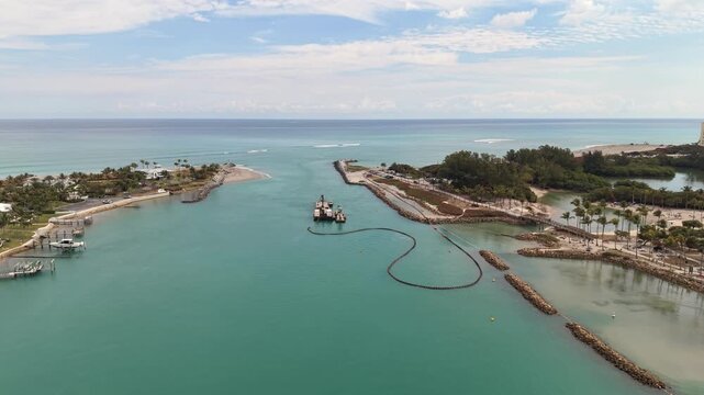Drone flying east away from the Jupiter Lighthouse in Jupiter Florida showing a barge moored near the mouth of the Jupiter Inlet and the Atlantic Ocean in the distance.