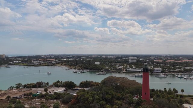 Drone flying south past the Jupiter Lighthouse toward the Jupiter Inlet showing people on the viewing platform after climbing the light with DuBois Park and marinas in the distance.