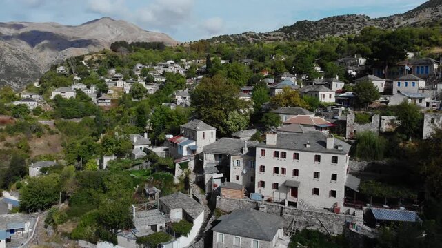 Stone houses dot a lush mountainside in Kalarrytes, Greece. The serene landscape offers a glimpse into traditional Greek architecture. Ideal for travel and cultural documentaries.