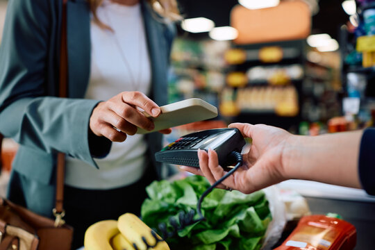 Close up of woman paying with smart phone in supermarket.