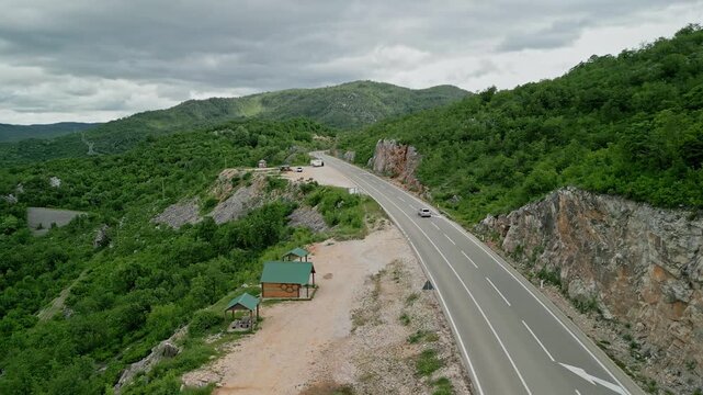 Slansko Lake, Montenegro - 05 29 2025: Drone still video of a winding asphalt road through lush, mountainous terrain in Ponikvica, with cars, rocky cliffs, forested valley and rustic wooden structures