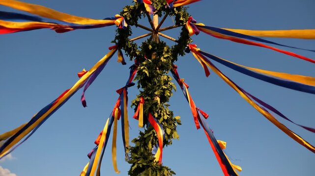 Maypole decorated with colorful ribbons and leaves in a sunny green field
