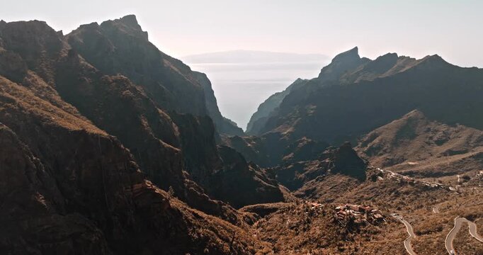 Impressive Masca valley landscape in Tenerife, featuring steep mountains, winding roads, and vast ocean stretching towards the horizon. Travel destination. Dramatic landscape. Aerial view drone flight