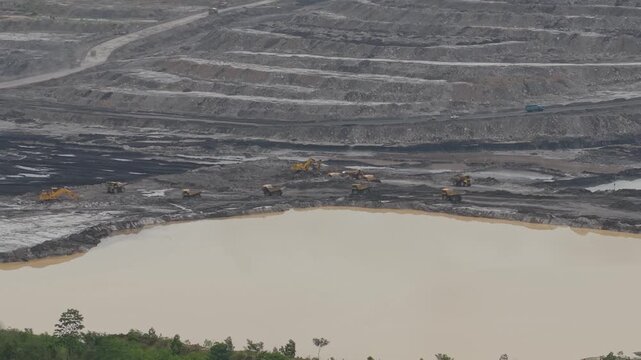 Aerial view of excavator and coal hauling truck activity, near a very deep excavation pit
