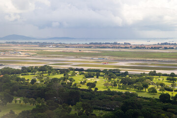 Obraz premium Commercial airplane taxiing on the runway at Changi Airport in Singapore. Green golf course and coastal landscape under a cloudy sky.