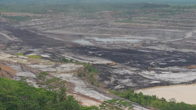 Aerial view of excavator and coal hauling truck activity, near a very deep excavation pit
