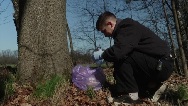 Horizontal shot of a man crushing a plastic bottle and cleaning up the forest. Successful waste collection and recycling concept.