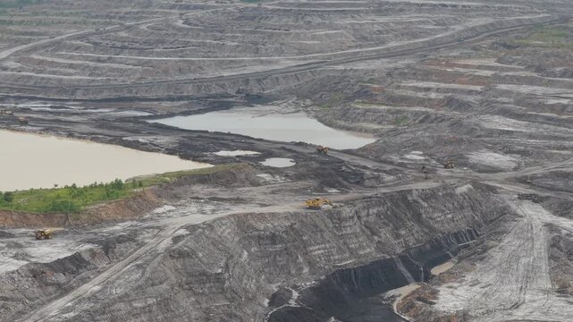 Aerial view of excavator and coal hauling truck activity, near a very deep excavation pit