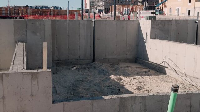 Slow motion pan across poured concrete walls and excavated foundation area on active jobsite.