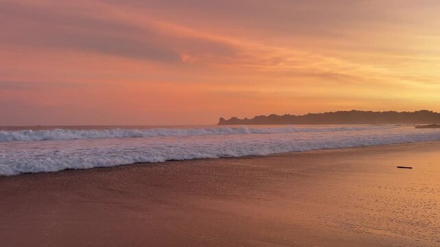 Golden sunset over a tropical beach with gentle ocean waves and silhouettes creating a calm and peaceful seaside atmosphere. located at Sendiki beach East Java, Indonesia