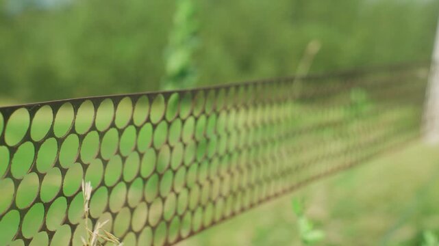Perforated Metal Fence In Meadow Circular Hole Pattern Creates Rhythmic Texture, Shallow Focus On Panel Edge With Sunlight Filtering Through Greenery, Industrial Detail Meets Pastoral Backdrop, Gentle