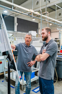 Two men discussing in a production hall with machinery in the background
