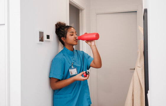 Nurse assistant in uniform drinking water on break at home