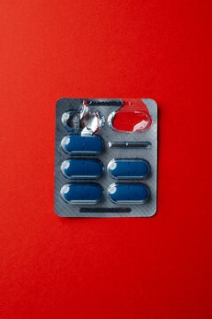 Blue capsule tablets in aluminum blister pack on red background