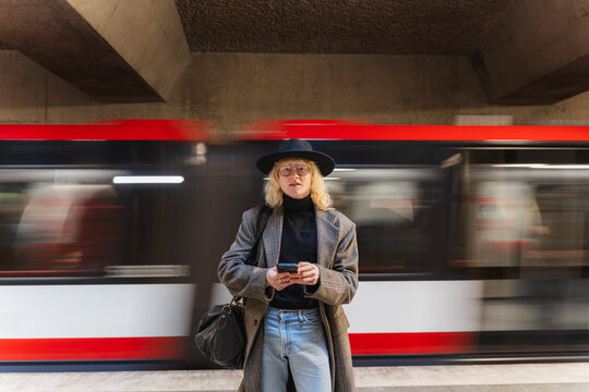 Commuter waiting with smartphone on urban subway platform indoors