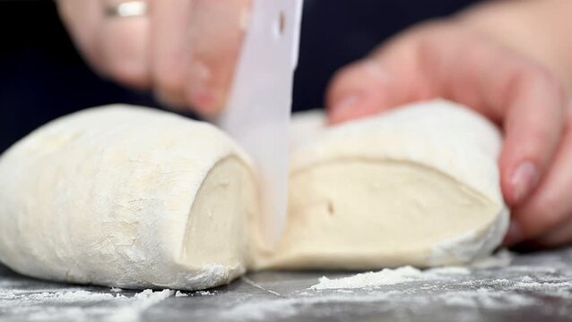 Hands of a person cutting and shaping dough on a floured surface, demonstrating the process of preparing bread in a cozy kitchen environment
