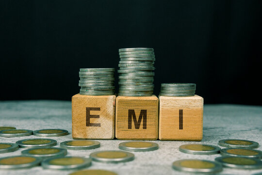EMI word on a wooden cube with a stack of coins. Financial Investment Concept.