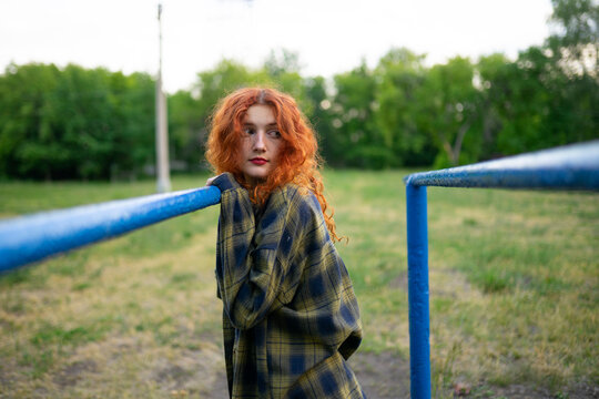 Woman with red curly hair in plaid shirt at old playground outdoors