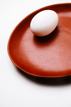 White egg on brown ceramic plate in minimalist studio setting