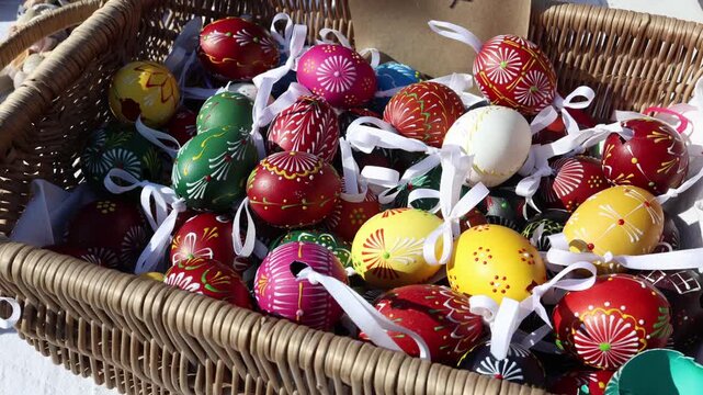 Easter painted eggs with traditional patterns in wicker basket tied with white ribbons displayed at outdoor market bright sunlight highlights colorful festive details