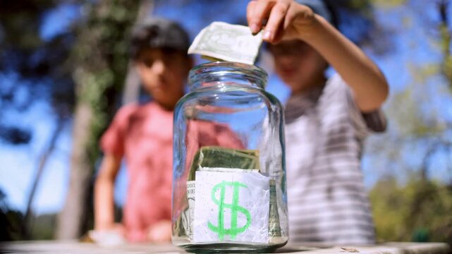 Children learning financial responsibility by putting us dollar bills into a save jar, symbolizing early investment, savings for the future, and economic education