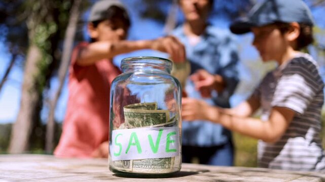 Children learning financial responsibility by putting us dollar bills into a save jar, symbolizing early investment, savings for the future, and economic education