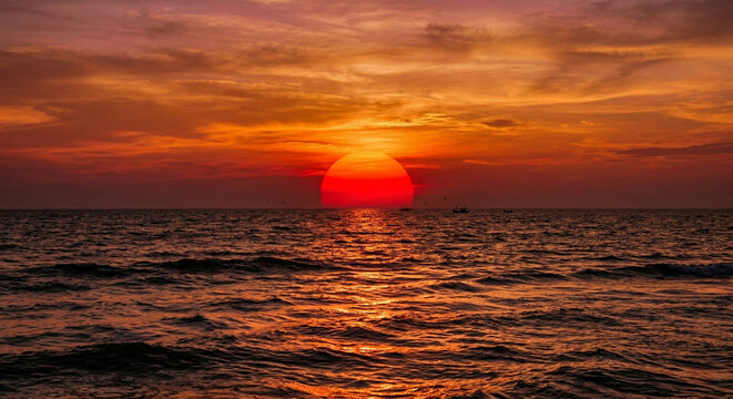 Big red sun setting over the ocean horizon with dramatic orange sky.
