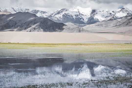 Panorama in the Tien Shan Mountains with a high plateau and rocky mountains, with a lake in the foreground, reflecting the mountain peaks and clouds, for the background