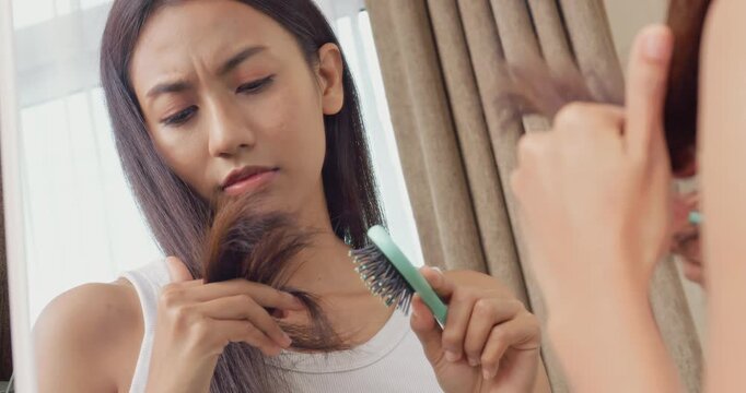 Beautiful Asian woman with tanned skin brushing hair and looking at damaged split ends with worried face.