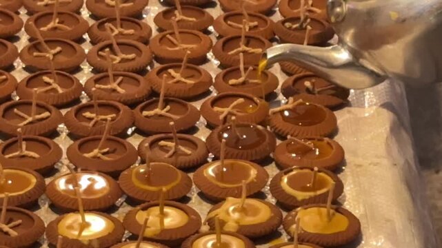 Video of wax pouring into small clay lamps for candle making showing traditional craft process and preparation