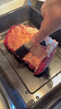 Vertical video social media - Closeup overhead shot of a hand using a pair of tongs to lower an uncooked topside joint of beef into a smoking hot oven baking tray, ready for cooking.