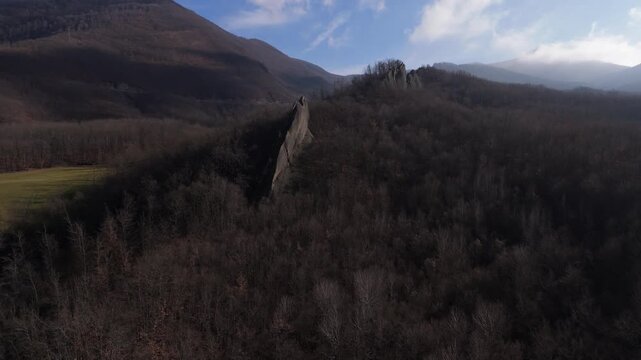 Zoom in aerial focusing on sharp Salti del Diavolo rock formation rising from forest.