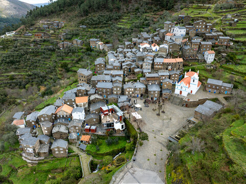 Aerial view of the historic village nestled in the valley, with its distinctive schist stone houses and the bright white church standing out, Piodao, Arganil, Portugal.