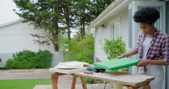Woman in flannel placing green fabric on patio bench, stapling frame preparing canvas, copy space
