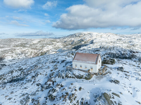 Aerial view of a solitary white building with a red roof amidst a snow-dusted, rocky landscape under a cloudy sky, Lagoa Comprida, Sao Romao, Serra da Estrella, Portugal.