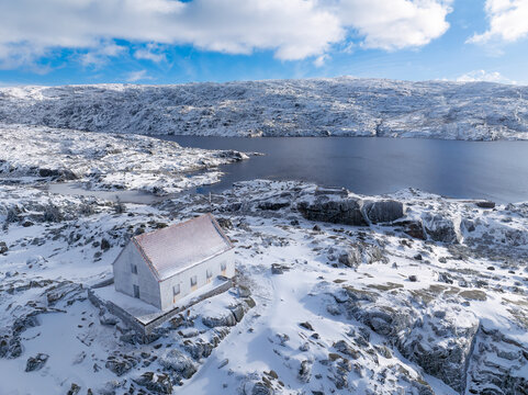 Aerial view of a solitary white building, embraced by snow-dusted rocks, stands sentinel over the tranquil, deep blue lake, Lagoa Comprida, Sao Romao, Portugal.