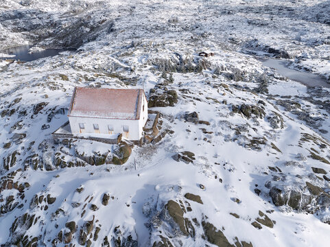 Aerial view of a white building with a red roof standing out against the snow-covered, rocky landscape, Lagoa Comprida, Sao Romao, Serra da Estrella, Portugal.