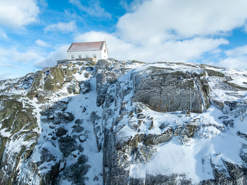 Aerial view of a stark white building perched atop a snow-dusted, rocky peak under a bright, scattered sky, Lagoa Comprida, Sao Romao, Serra da Estrella, Portugal.