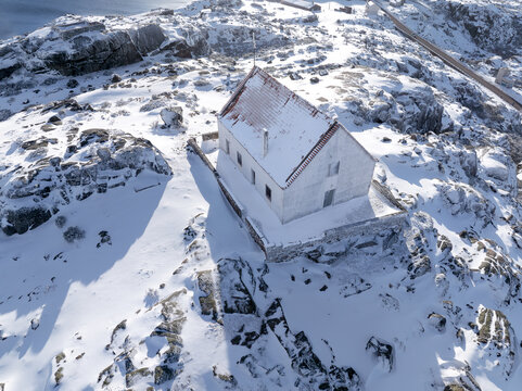 Aerial view of a snow-covered building with a red roof amid a stark, white landscape, Lagoa Comprida, Sao Romao, Serra da Estrella, Portugal.