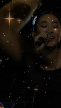 Vertical video: Singer starting song, singing into mic while crowd arms blocking, star overlay