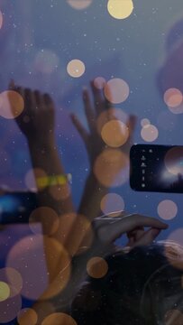 Vertical video: Event guest hand bringing phone up, recording hands rising, yellow band amid bokeh