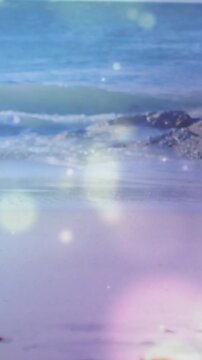 Vertical video: Woman entering and walking left by sea for tech as pink bokeh over her with phone
