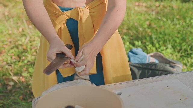 Woman slicing onion outdoors camping skillet, steady hands guiding knife over cutting area, picnic table with bowl and pan, sizzling anticipation for camp meal, bright grassy setting, efficient prep